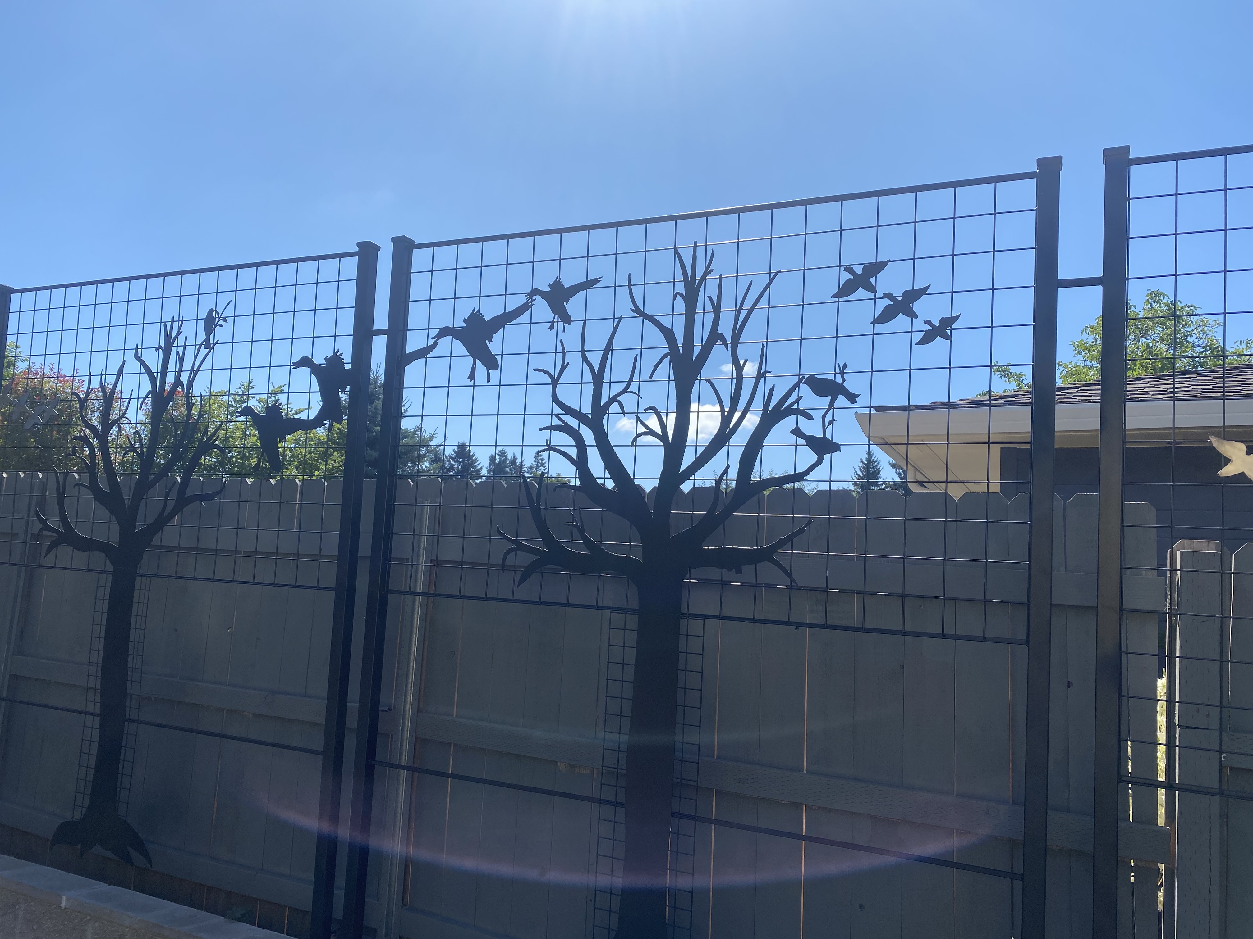 A tall custom iron fence, with birds pirched on a tree and birds flying.  The scene contiunes on each fence panel.